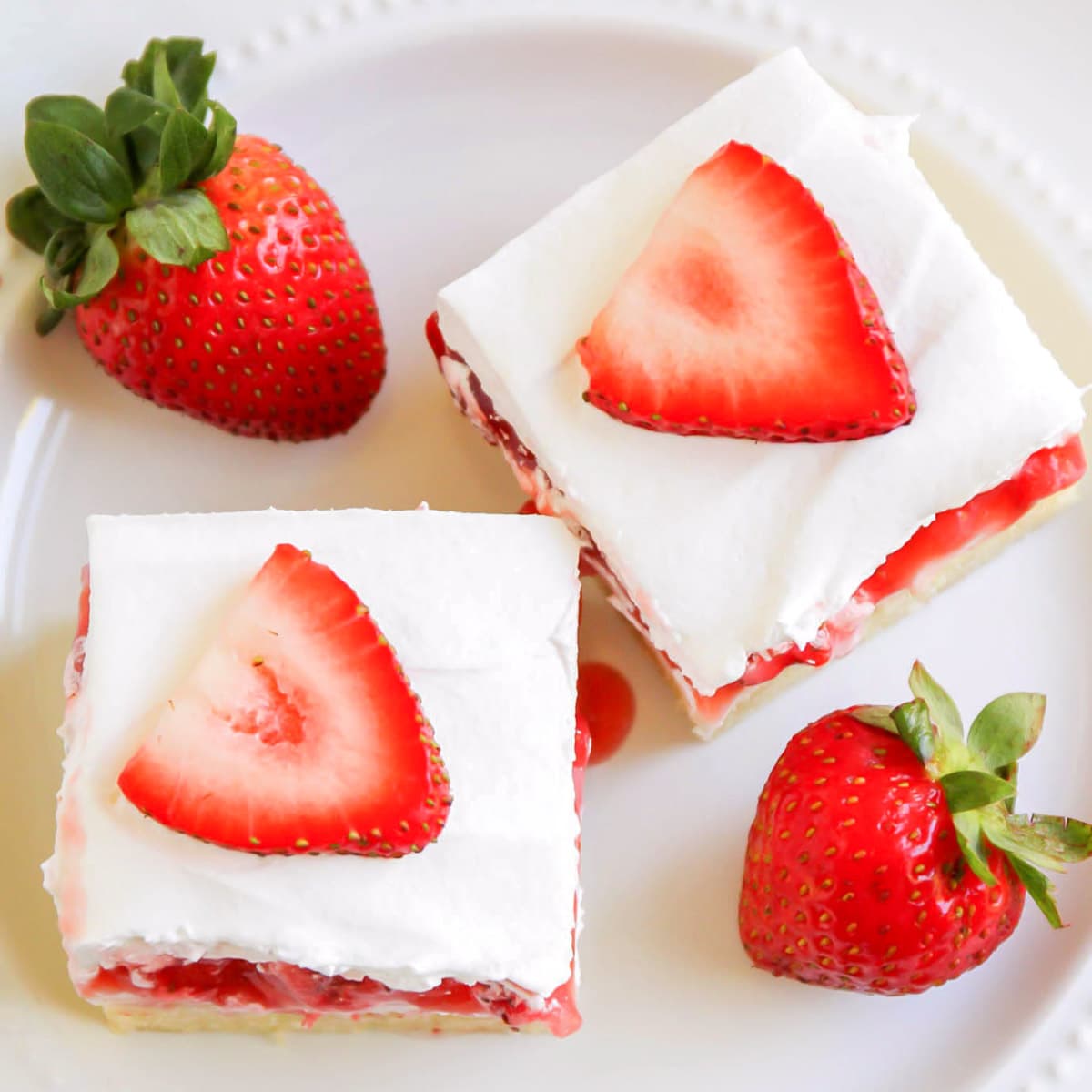 甜点条食谱——草莓奶油芝bob综合手机客户士条，上面放草莓片，旁边放两个草莓，放在白色盘子里。