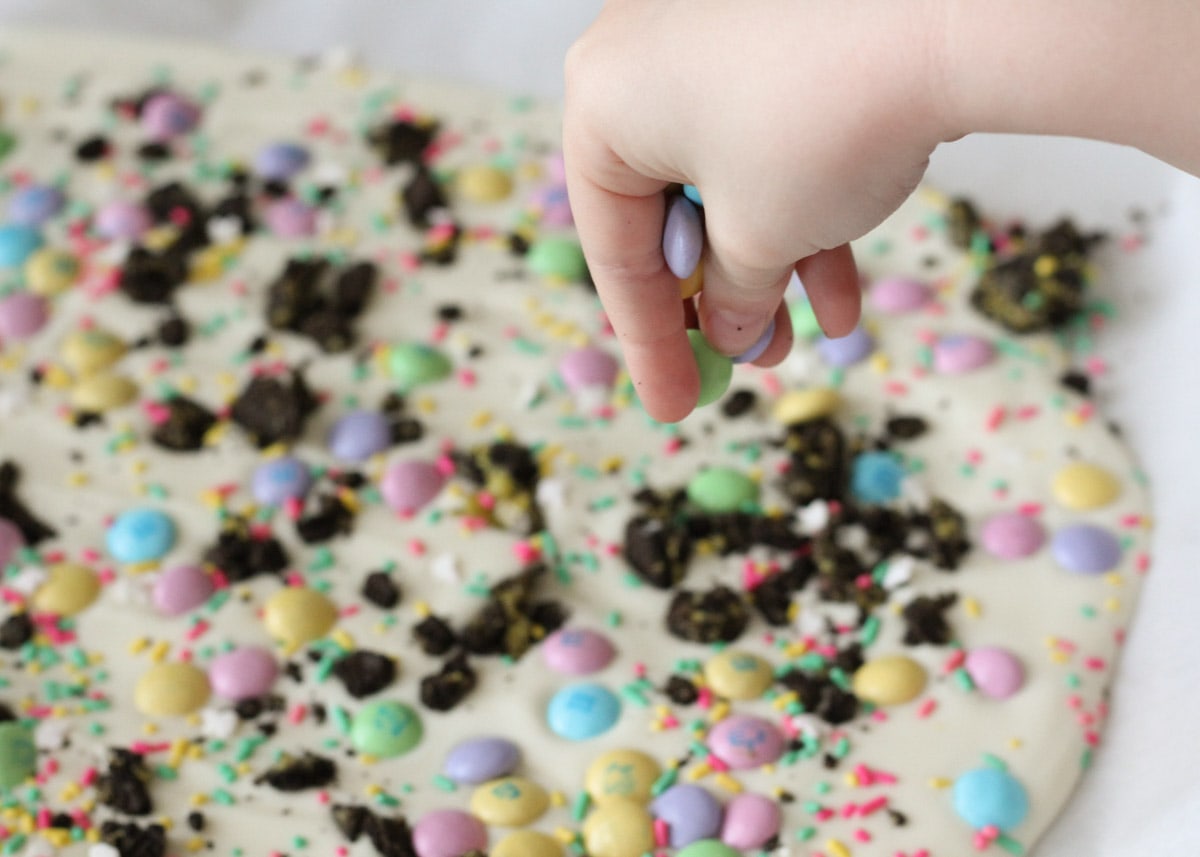 A hand sprinkling candy on top of oreo bark