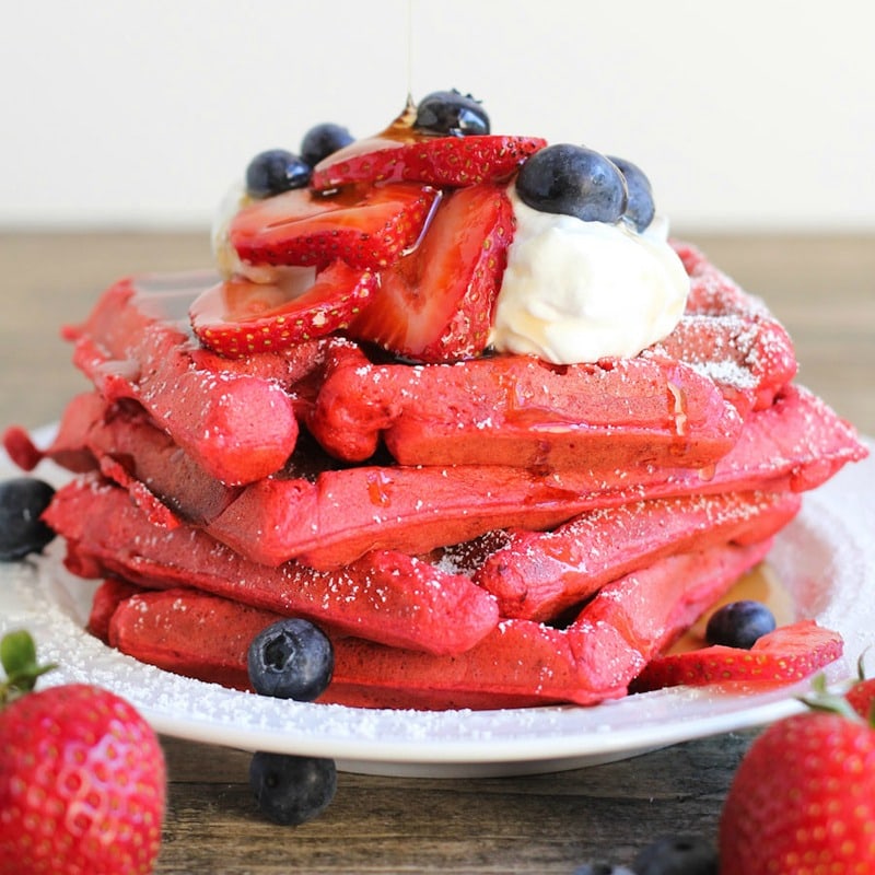 白色盘子里的一叠红丝绒华夫饼上面放着草莓和蓝莓。