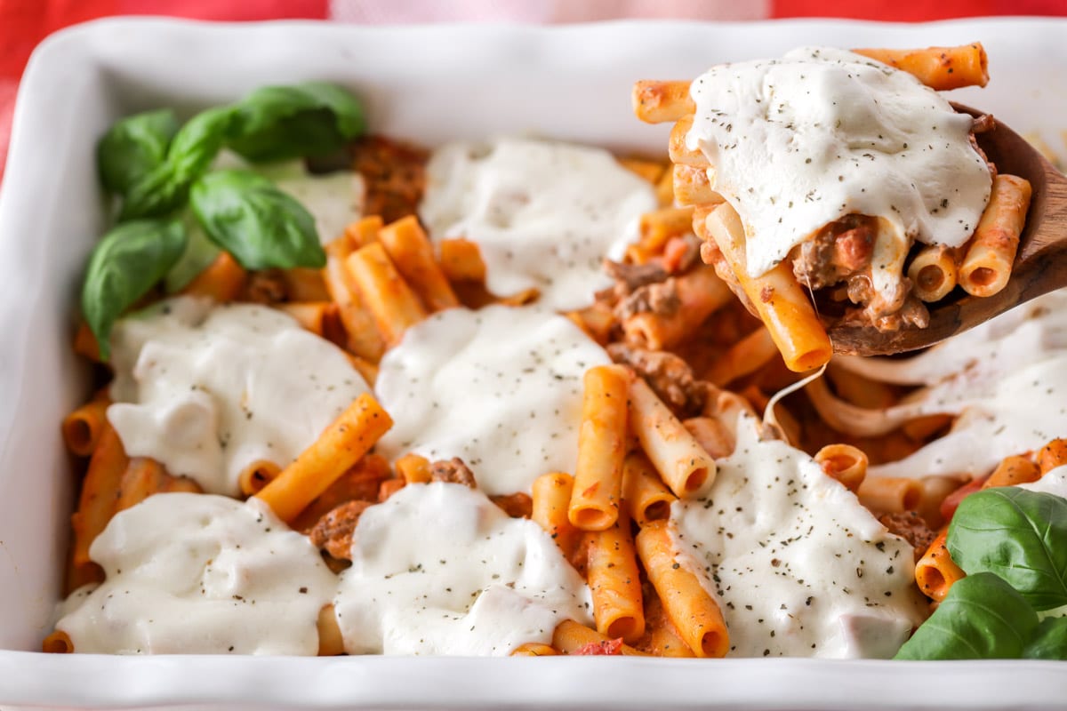 简单的意大利面食谱——bob综合手机客户用勺子从砂锅盘中舀出烤好的意大利面。