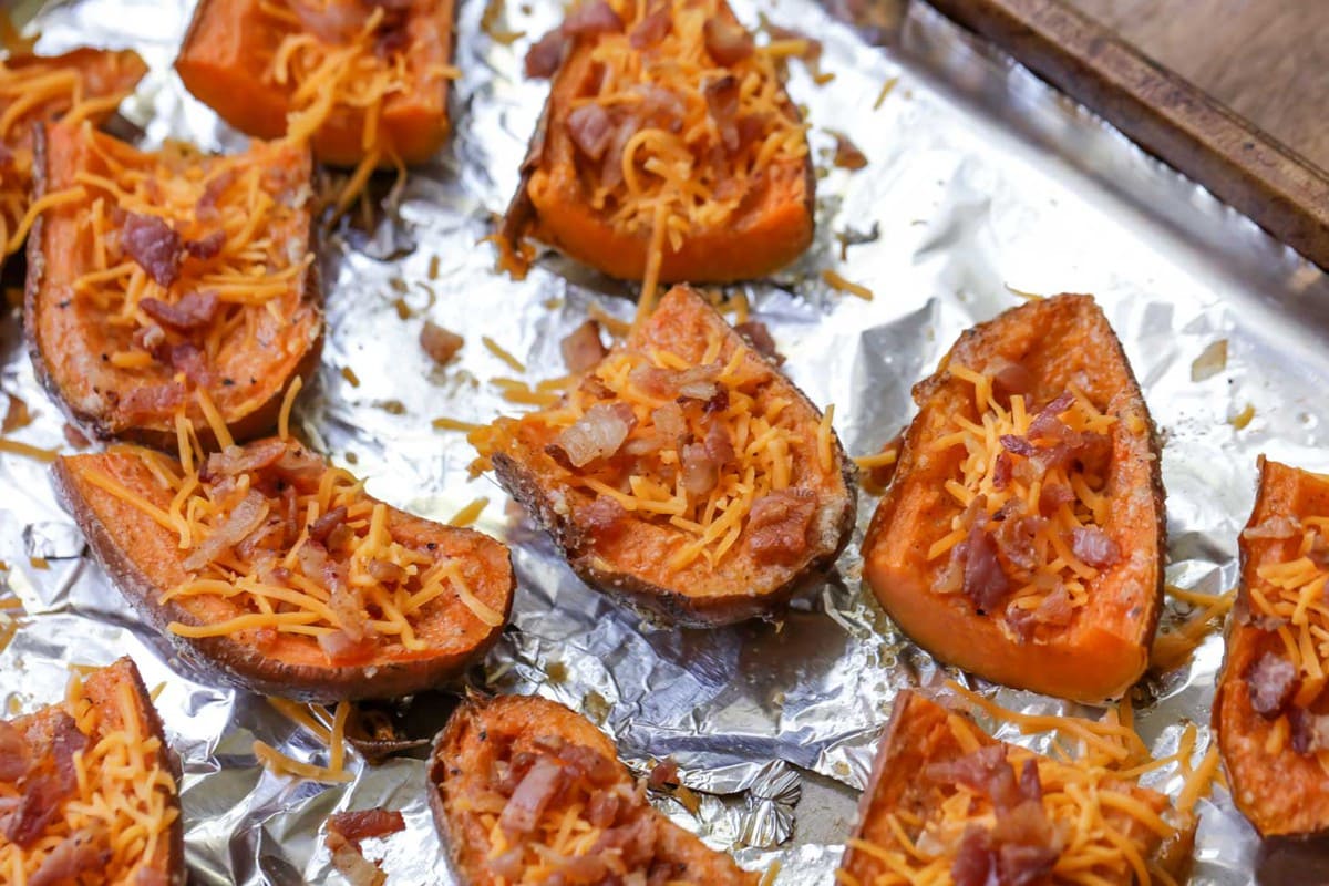 健康的开胃菜——烤过的甘薯皮，上面撒上切达奶酪丝和切碎的培根，放在锡箔衬里的烤盘上。