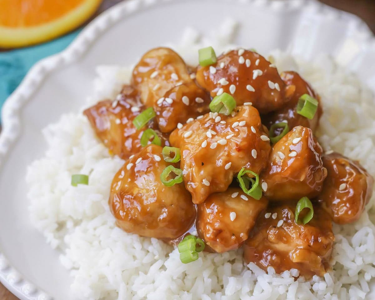 亚洲晚餐食谱——在白盘子里bob综合手机客户的白米饭上，撒上芝麻和葱丁的橙鸡。
