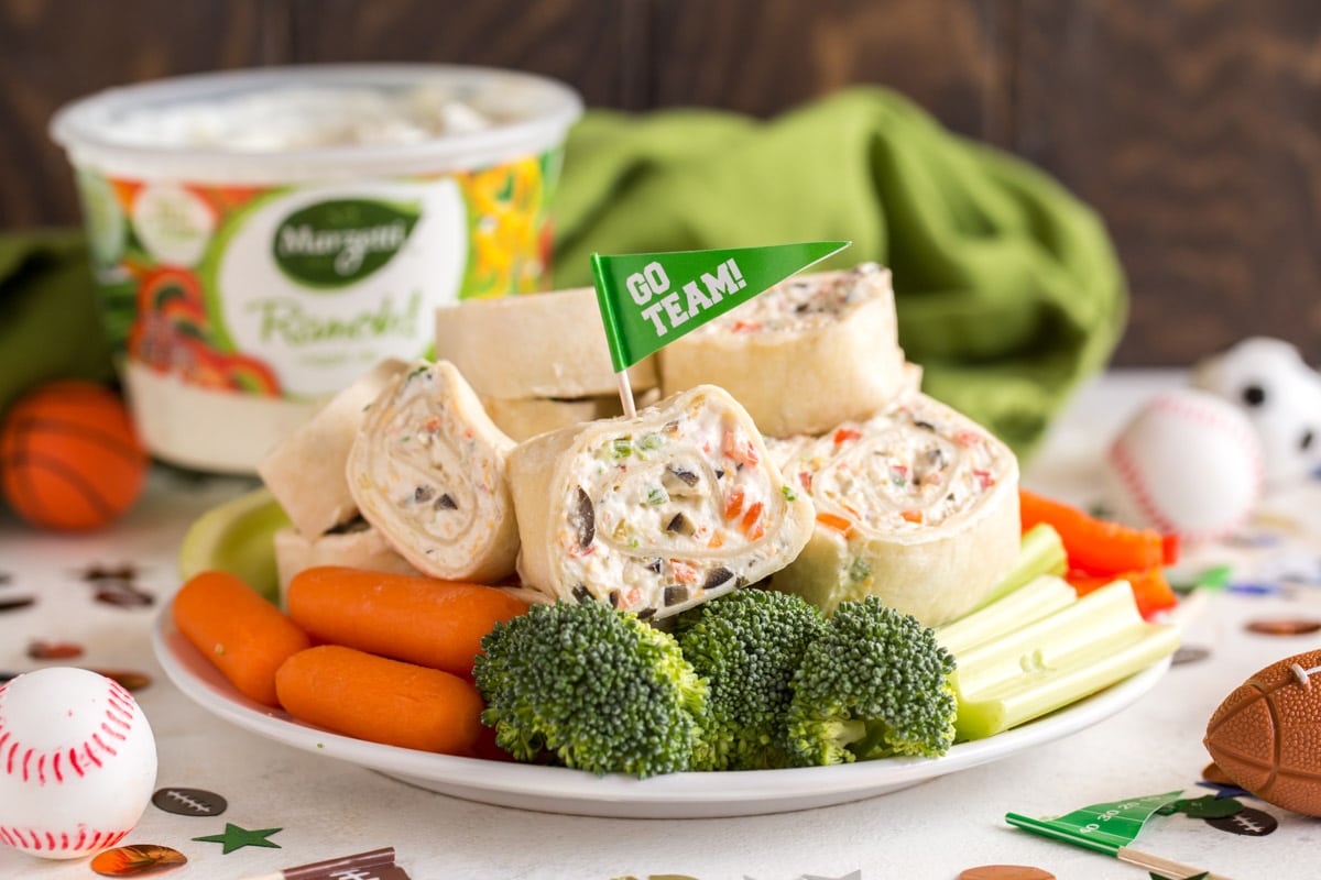 简单的开胃菜-蔬菜玉米饼卷，一个卷上插着一个国旗牙签，上面写着“团队”，周围是白色盘子上的生蔬菜。