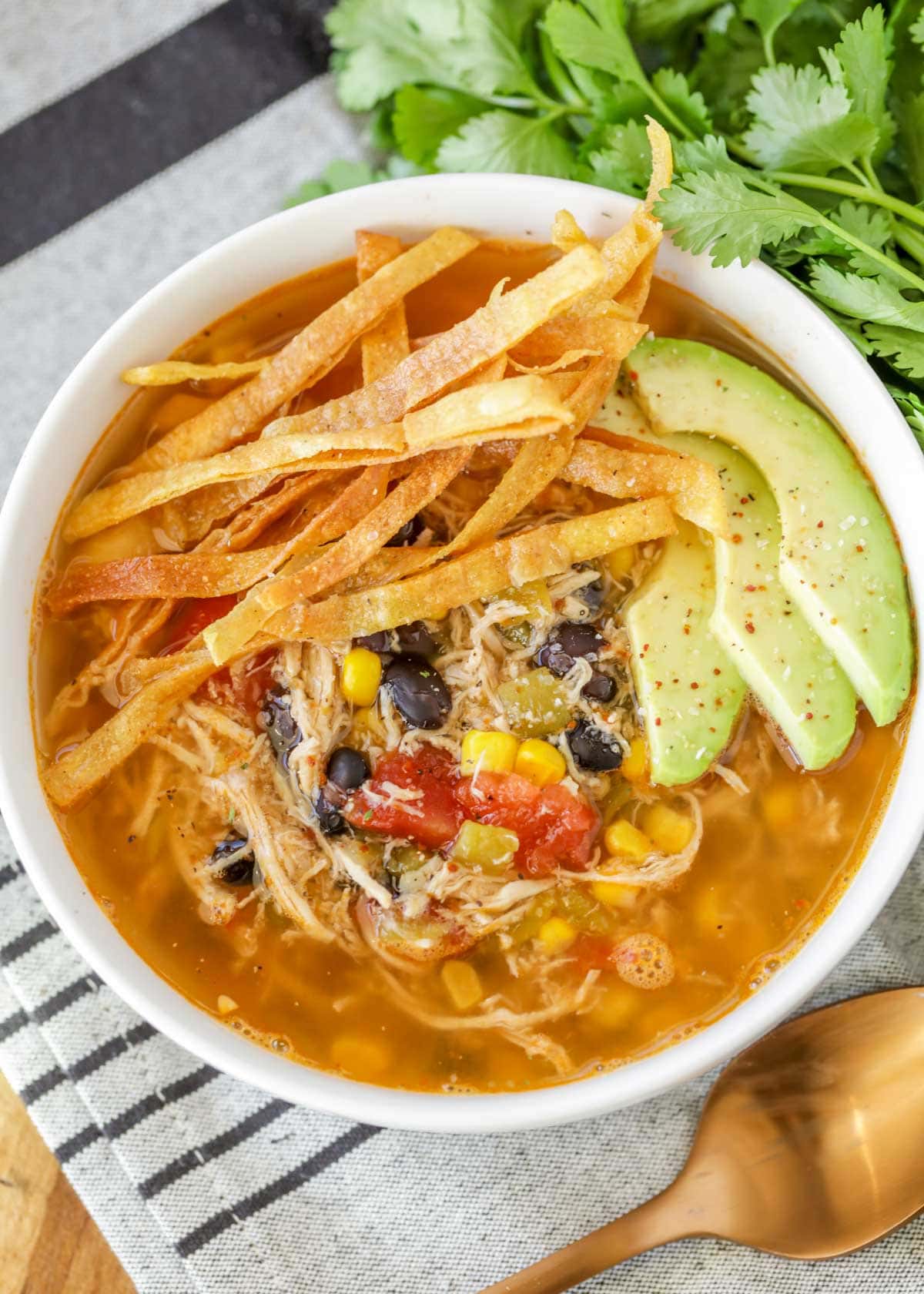Chicken Tortilla Soup recipe in bowl with tortilla strips and avocado on top.