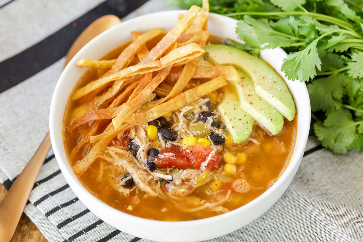 墨西哥汤食谱:一碗鸡肉玉米bob综合手机客户饼汤，淋上牛油果和玉米饼条。