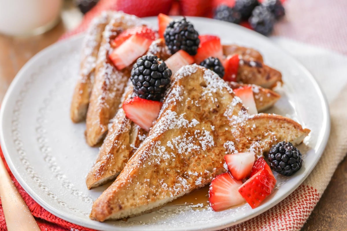 Easy Breakfast Ideas - French toast slices dusted with powdered sugar and topped with blackberries, strawberries, and syrup on a white plate.