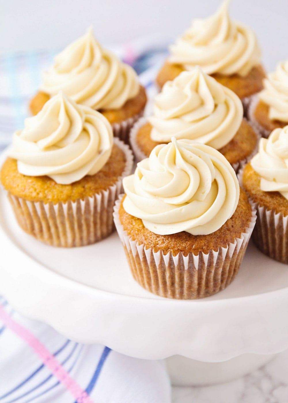 Carrot cake cupcakes recipe on white cake stand topped with brown sugar cream cheese frosting.