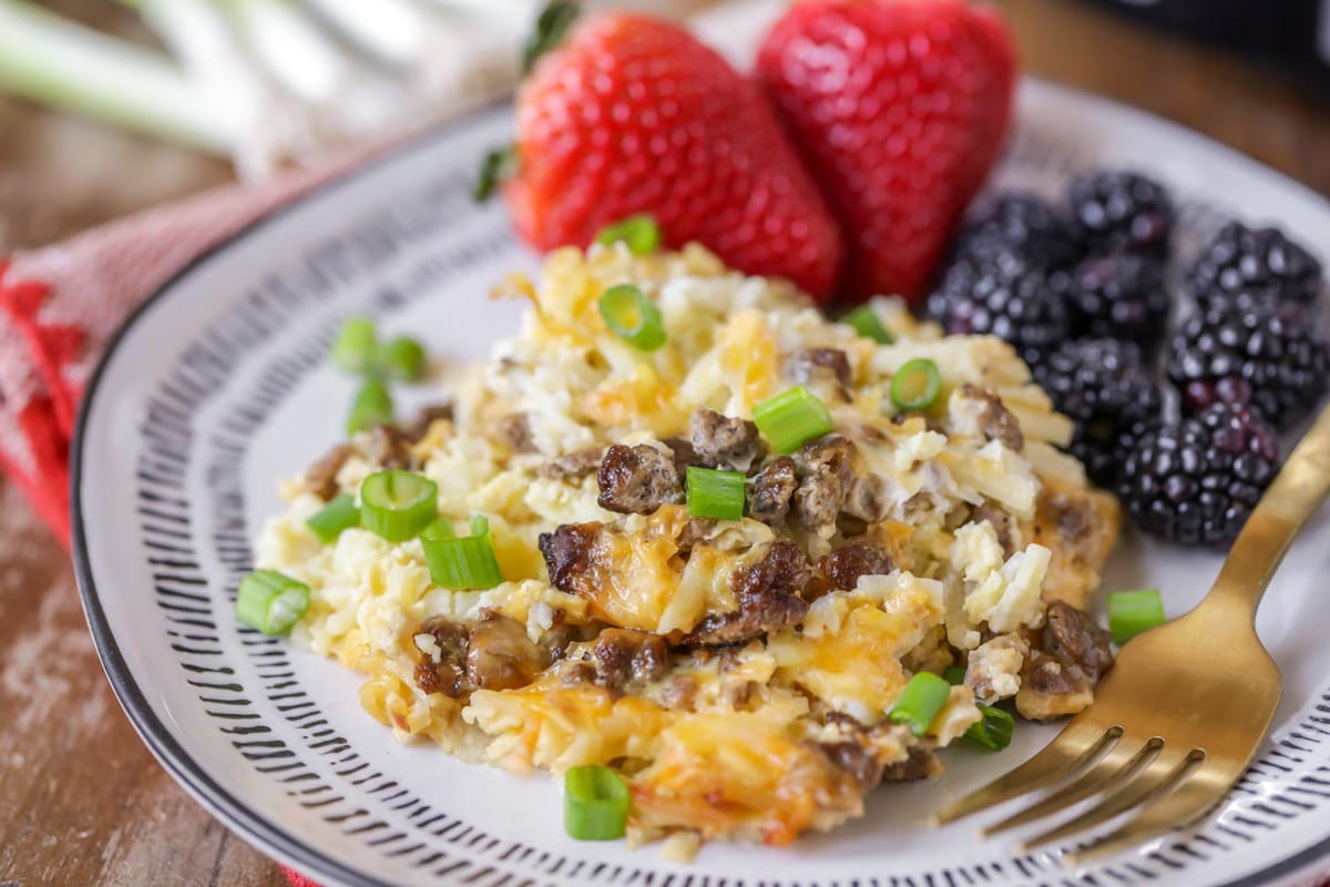 Easy Breakfast Ideas - crockpot breakfast casserole with a side of strawberries and blackberries on a blue and white plate with a gold fork resting on the plate.