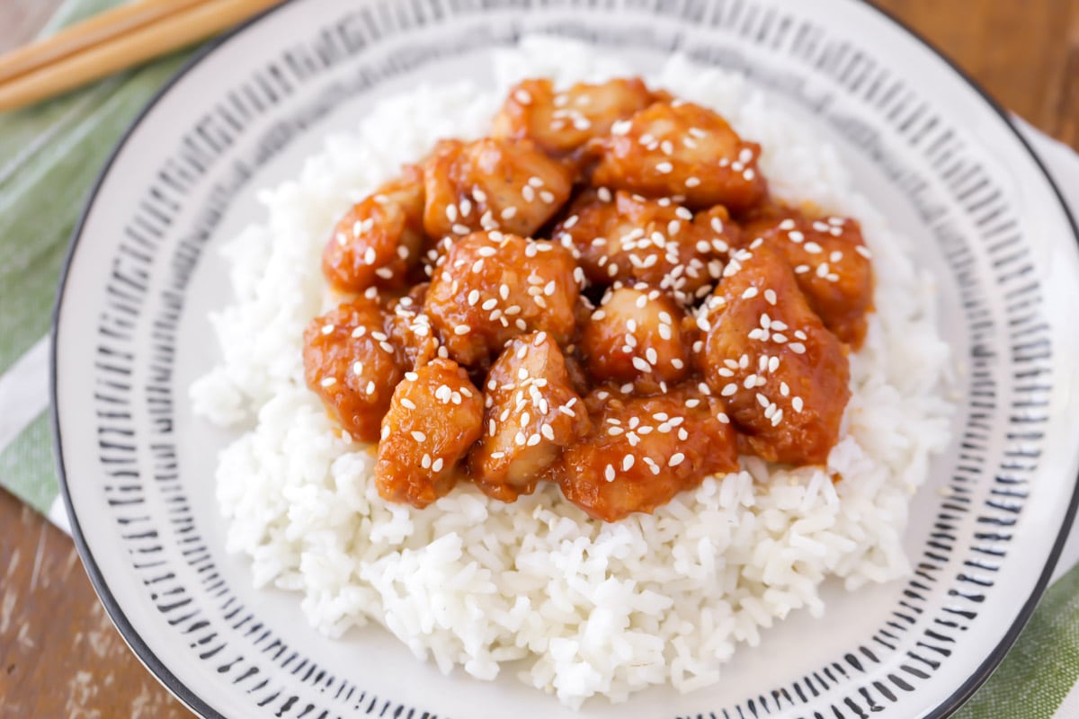 亚洲晚餐食谱——芝麻鸡放在bob综合手机客户白盘子里的白米饭上。