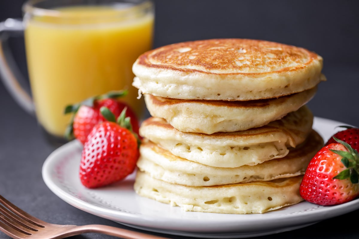 Easy Breakfast Ideas - A stack of fluffy pancakes garnished with whole strawberries on a white plate.