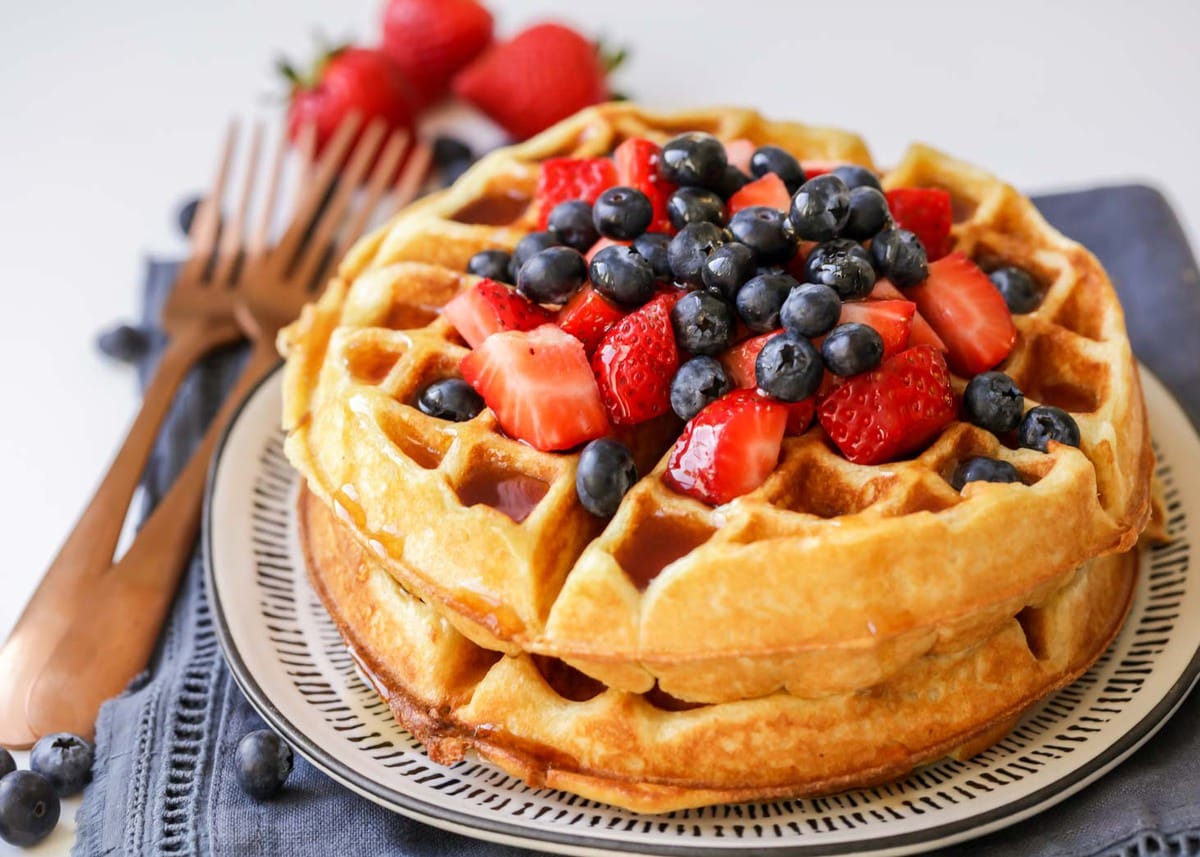 简单的想法——一堆白脱牛奶waffl早餐es topped with strawberries and blueberries on a white and blue plate.