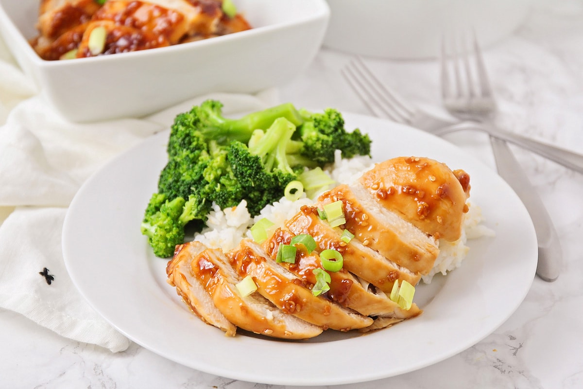 亚洲晚餐食谱——烤照烧鸡切bob综合手机客户片，放在白米饭上，配上西兰花，放在白盘子里。
