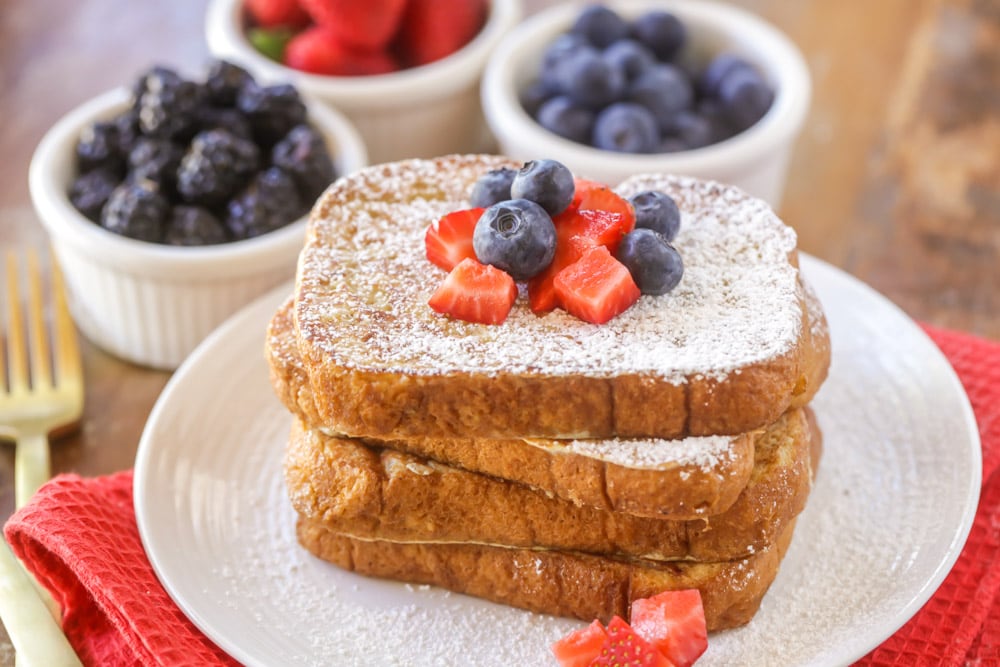 Easy Breakfast Ideas - A stack of fluffy French toast dusted with powdered sugar and topped with strawberries and blueberries on a white plate.