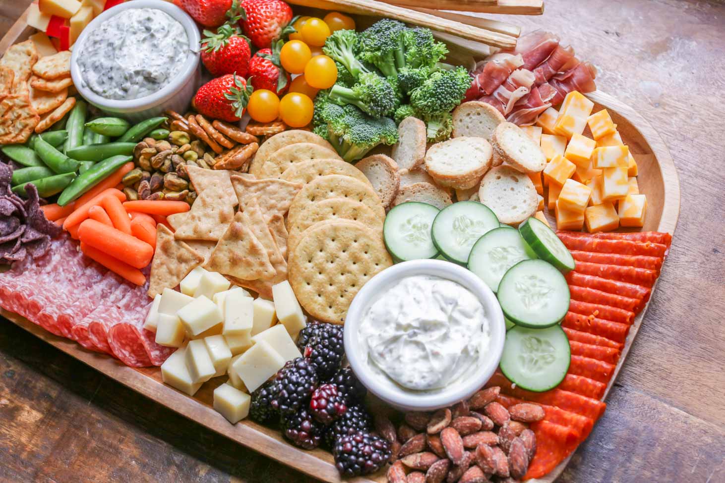 手指食物开胃菜——一个装满水果、蔬菜、饼干和蘸酱的熟食板。