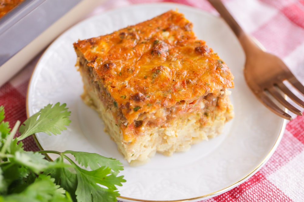 Easy Breakfast Ideas - a slice of Mexican breakfast casserole on a white plate with a metal fork resting on the side of the plate.