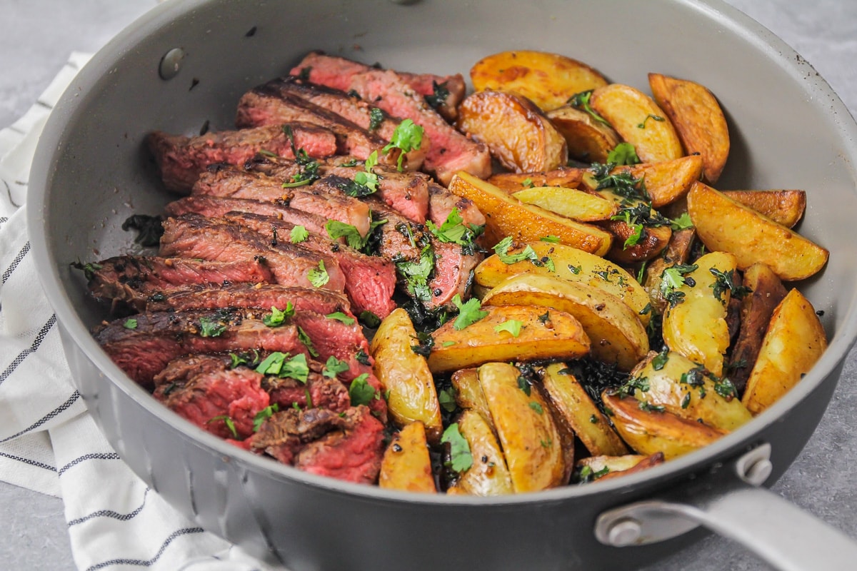 冬季晚餐建议:牛排和土豆放在煎锅里，上面撒上切碎的欧芹。