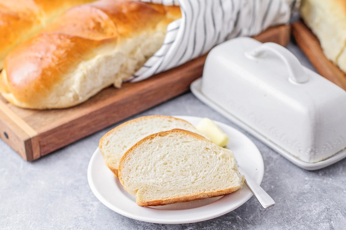 新鲜出炉的切片法国面包配黄油，放在白盘子里。bob综合手机客户