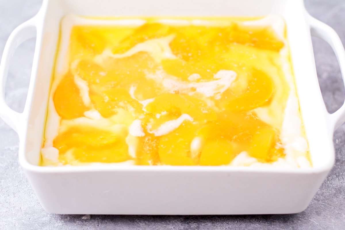 桃子罐头倒在面糊和融化的黄油上，放在烤盘里。