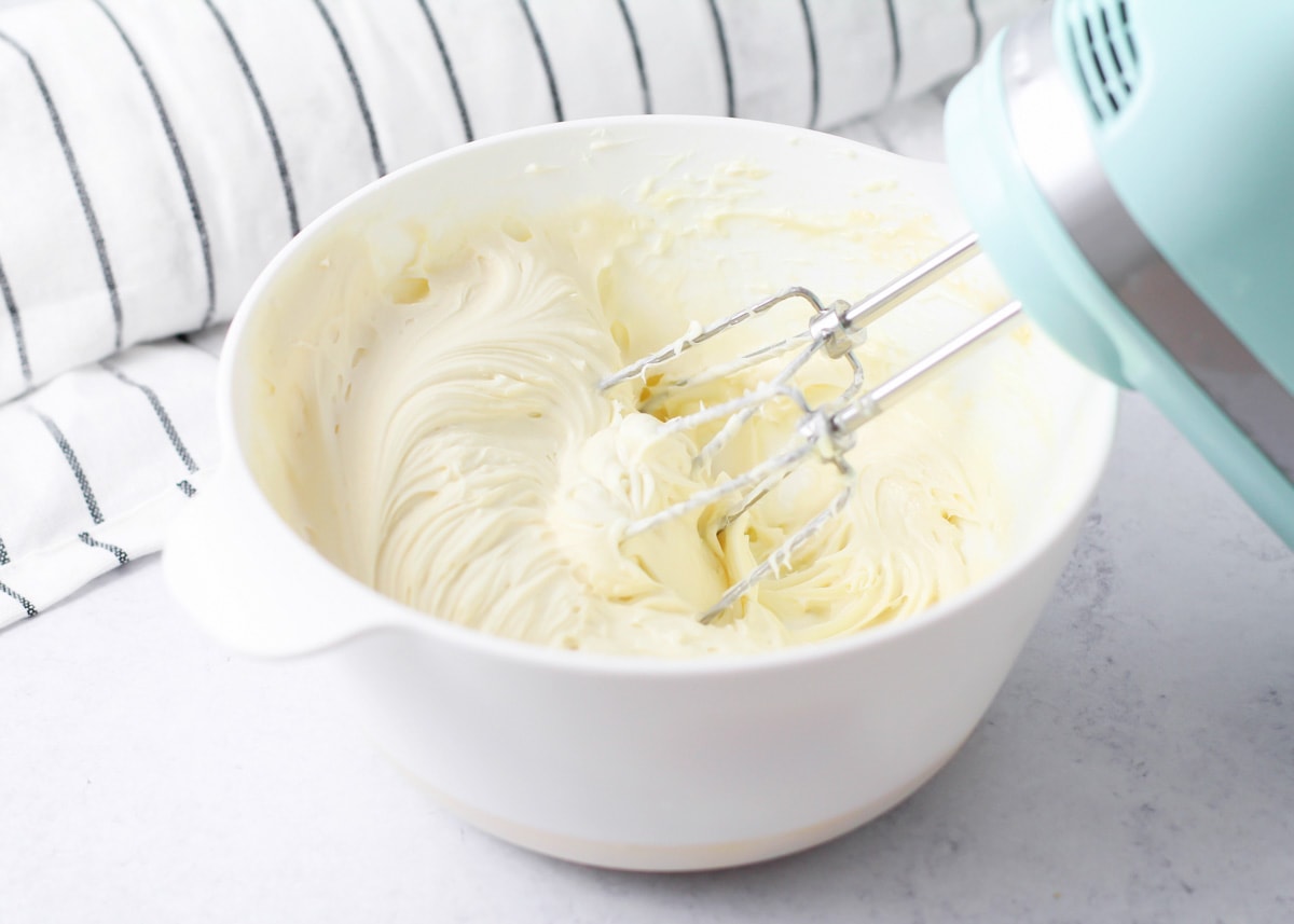 搅拌碗装满奶油乳酪糖霜的南瓜卷。