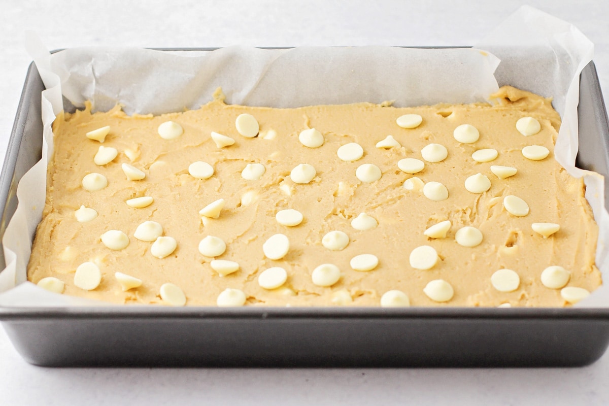 金色蛋糕面糊上白巧克力片，放在金属烤盘里。